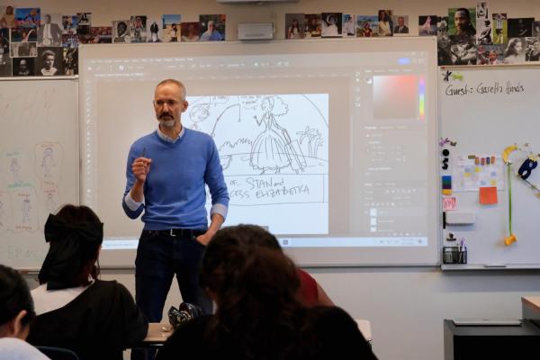 Gareth Hinds stands in front of an 8th grade English class, his artwork on display behind him.